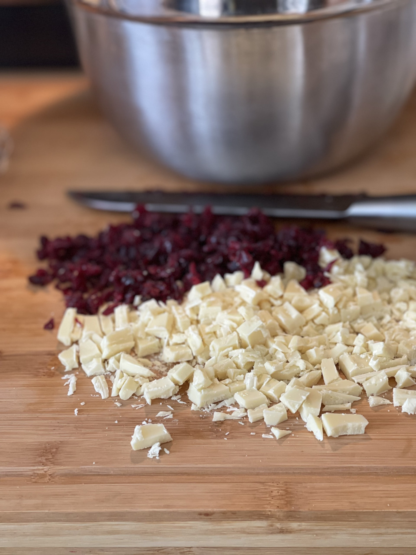 Chopped cranberries and white chocolate on a cutting board, prepped for a batch of cookies